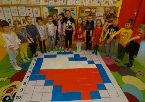 Grupa dzieci stoi wokół maty edukacyjnej na której z kolorowych płytek ułożona jest mapa Polski.